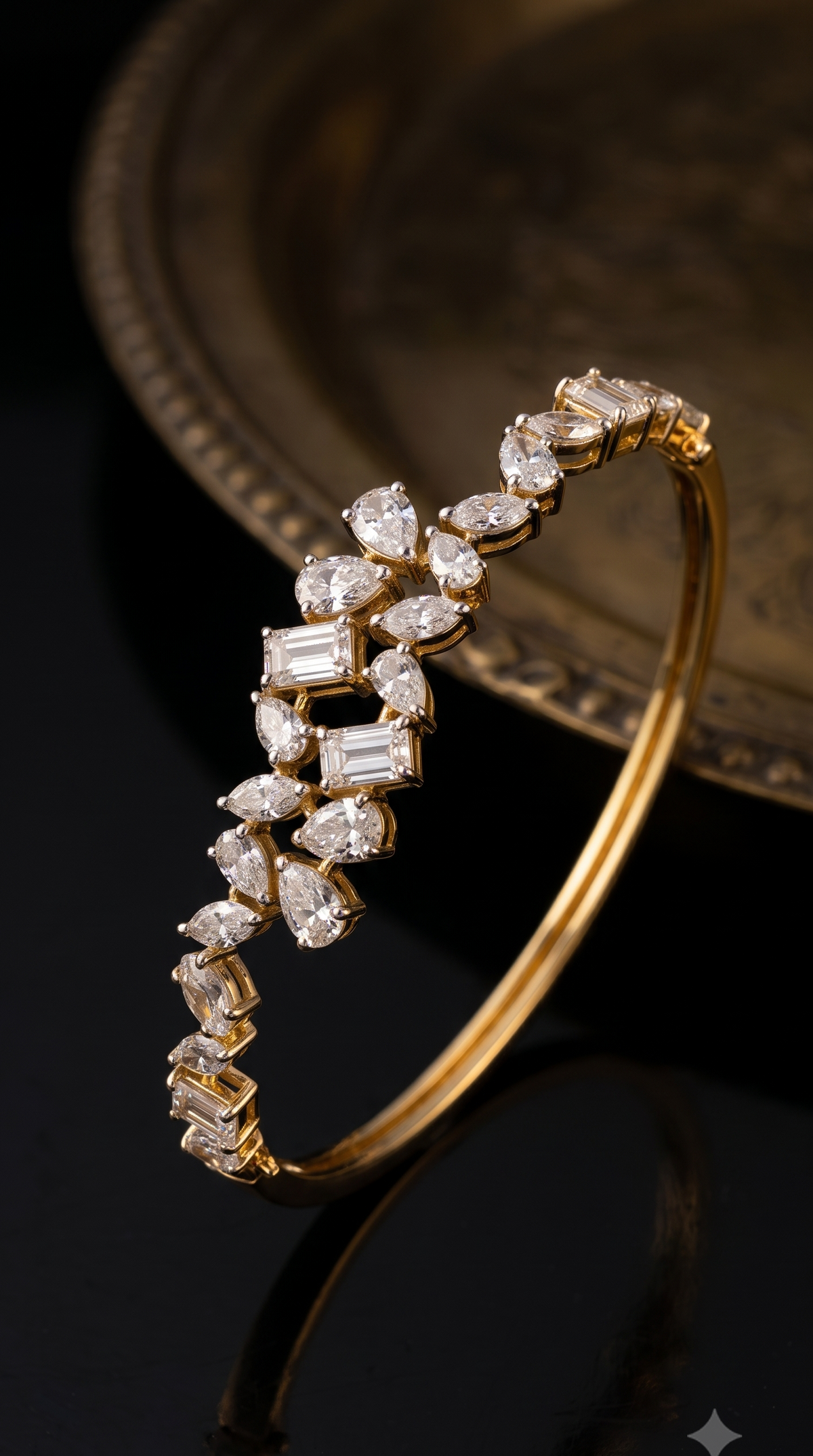 A gold bangle bracelet adorned with a cascading arrangement of clear rectangular and marquise-cut gemstones, photographed on a glossy black surface with a blurred antique gold plate in the background.