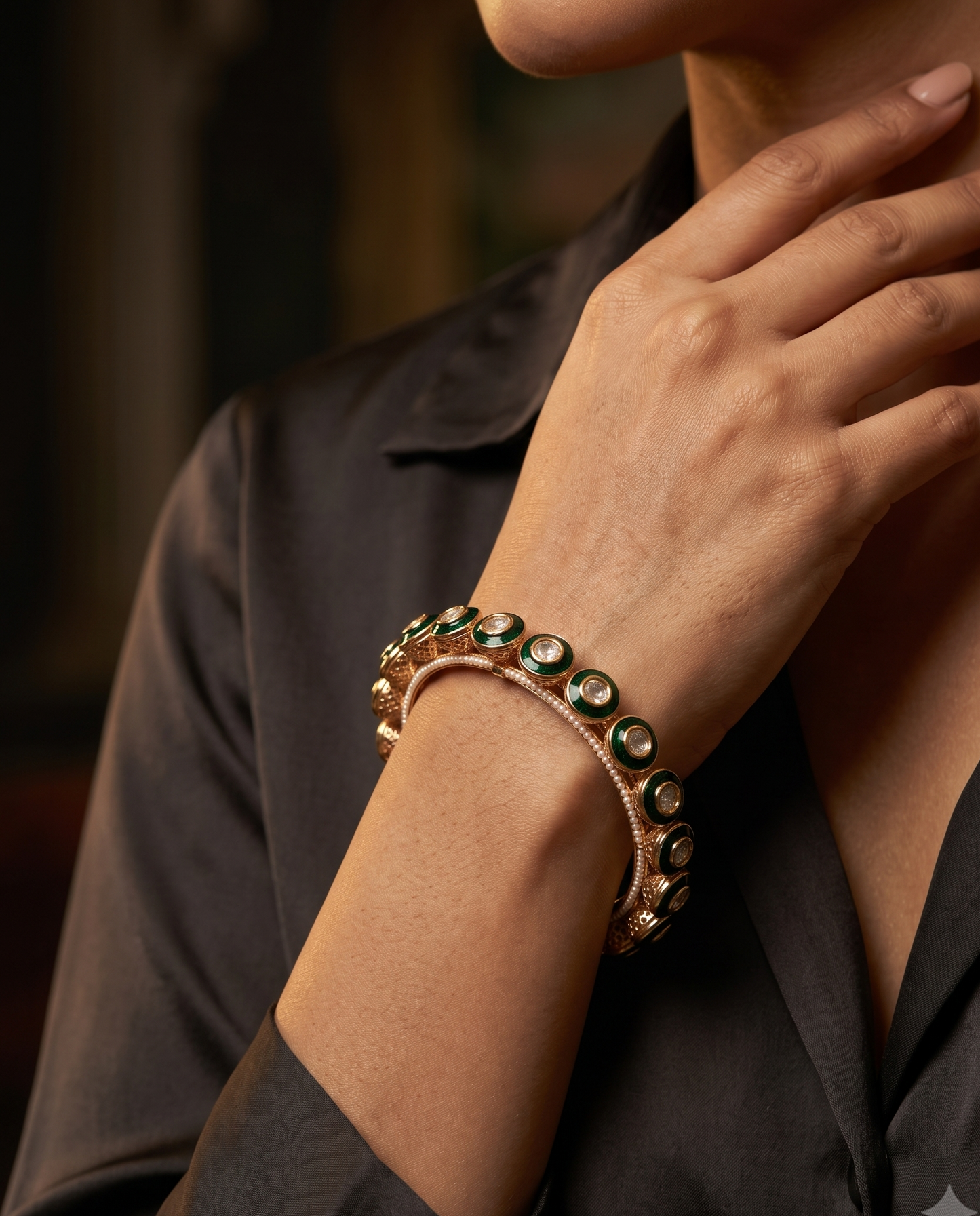 A close-up lifestyle shot of a model wearing a double-layered cuff bracelet. The bracelet features a rose gold-toned base with round green gemstone accents, worn on the wrist of a person in a black satin shirt.
