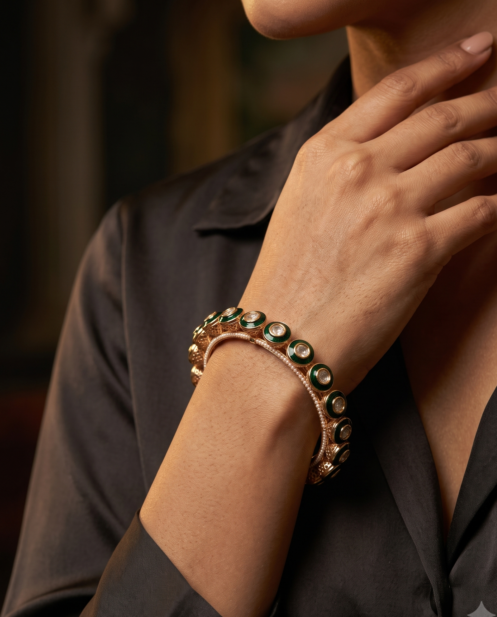 A close-up lifestyle shot of a model wearing a double-layered cuff bracelet. The bracelet features a rose gold-toned base with round green gemstone accents, worn on the wrist of a person in a black satin shirt.