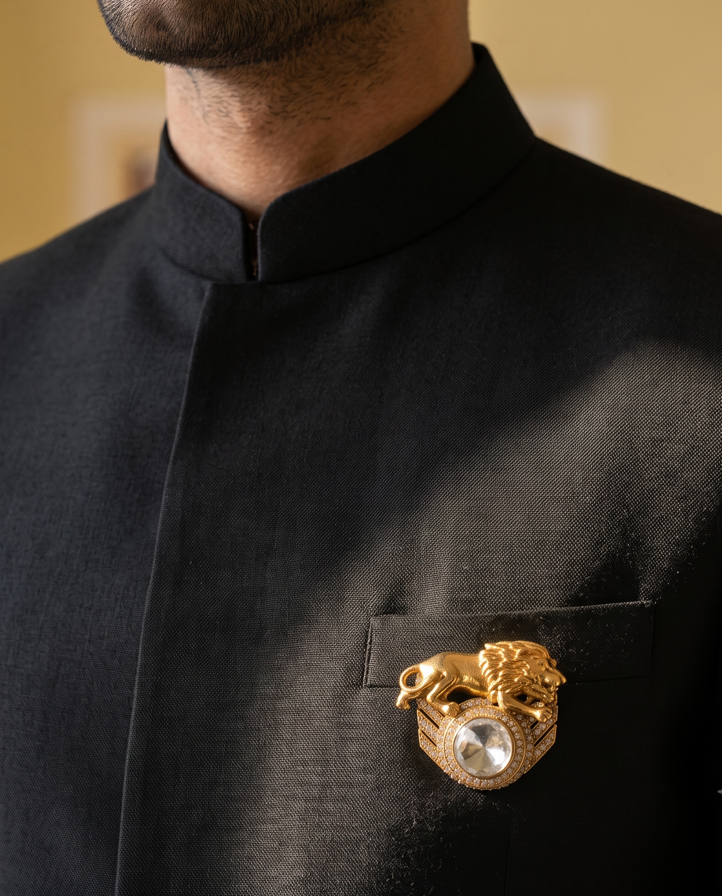 A close-up of a man wearing a black traditional high-collar jacket with a gold lion-and-dragon style brooch featuring a pearl center, pinned to the chest pocket.