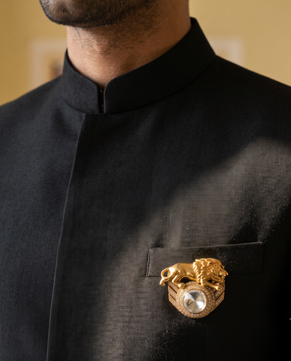 A close-up of a man wearing a black traditional high-collar jacket with a gold lion-and-dragon style brooch featuring a pearl center, pinned to the chest pocket.