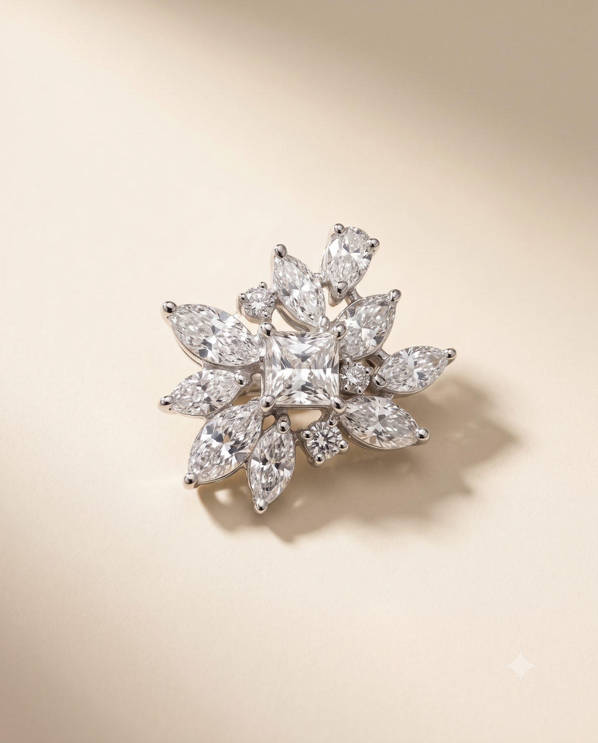 A floral cluster diamond brooch with a central princess-cut diamond surrounded by marquise and round diamonds in a silver-toned setting, photographed on a warm cream background.